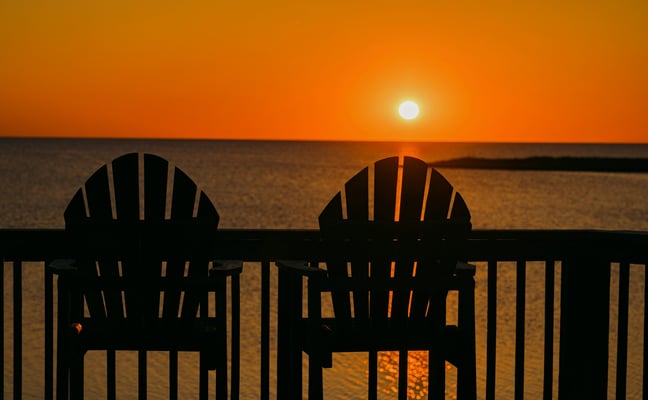 Two Adirondack chairs at sunset over calm ocean water